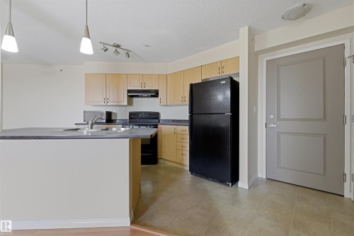 Open-concept kitchen featuring wood-finish cabinetry, dark countertops, and a black appliance suite - 407 11453 Ellerslie Road Sw, Edmonton, AB - Indoor Photo Showing Kitchen