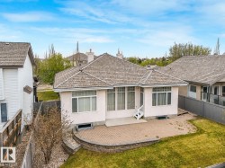 Rear exterior featuring a paver patio with a stone retaining wall, white siding, and multiple windows - 
