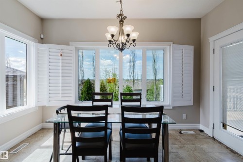 Dining area featuring a prominent window array with plantation shutters, tile flooring, and a decorative chandelier - 3412 Macneil Link, Edmonton, AB 