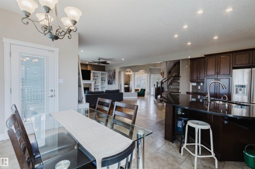 Open-concept living area featuring a kitchen island with dark countertops, wood-finish cabinetry, and stainless steel appliances - 3412 Macneil Link, Edmonton, AB 