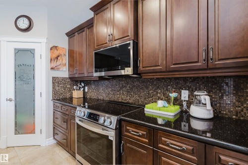 Kitchen featuring dark wood cabinetry, black countertops, a stainless steel range, and a mosaic tile backsplash - 3412 Macneil Link, Edmonton, AB 