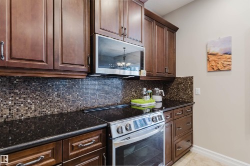 Kitchen featuring rich wood cabinetry, dark speckled countertops, and a mosaic tile backsplash - 3412 Macneil Link, Edmonton, AB 