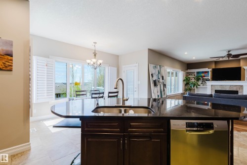 Kitchen island featuring a dark countertop, undermount sink with a gooseneck faucet, and a stainless steel dishwasher - 3412 Macneil Link, Edmonton, AB 