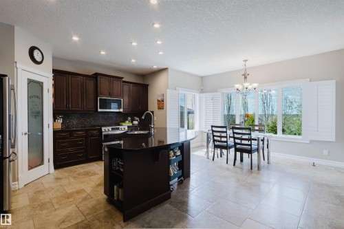 Kitchen featuring dark wood cabinetry, a central island with a solid surface countertop, and stainless steel appliances - 3412 Macneil Link, Edmonton, AB 