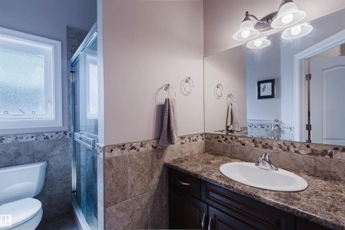 Bathroom featuring a dark wood-finish vanity with an integrated sink, a large mirror, and a four-light fixture - 3412 Macneil Link, Edmonton, AB 