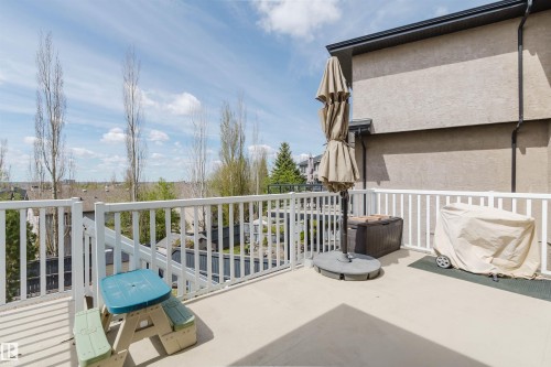 Spacious outdoor deck featuring a white railing system, stucco exterior, and a glimpse of the surrounding neighborhood rooftops and distant trees - 3412 Macneil Link, Edmonton, AB 