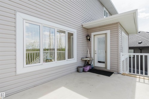 Exterior deck area featuring light-toned siding, a multi-pane window with white trim, a covered entryway with a glass-paneled door, and a white railing system - 3412 Macneil Link, Edmonton, AB 