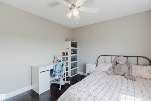 Bedroom featuring dark tile flooring, neutral wall tones, and a ceiling fan with integrated lighting - 3412 Macneil Link, Edmonton, AB 