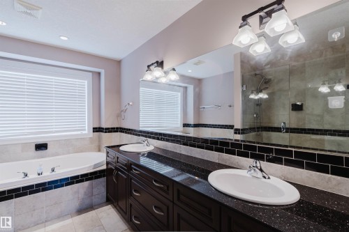 Bathroom featuring a dual vanity with a dark wood-finish cabinet and speckled dark countertops - 3412 Macneil Link, Edmonton, AB 