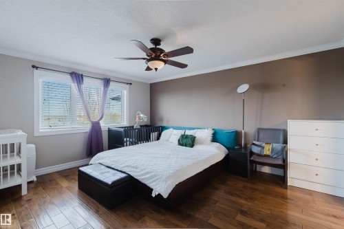 Spacious room featuring wood-finish flooring, a ceiling fan with integrated lighting, a large window with blinds, and crown molding - 3412 Macneil Link, Edmonton, AB 