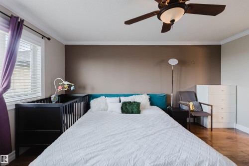 Bedroom featuring a ceiling fan with integrated lighting, crown molding, and wood-finish flooring - 3412 Macneil Link, Edmonton, AB 