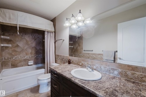 Bathroom featuring a dark wood-finish vanity with an oval undermount sink, a speckled countertop, and a large wall-mounted mirror - 3412 Macneil Link, Edmonton, AB 