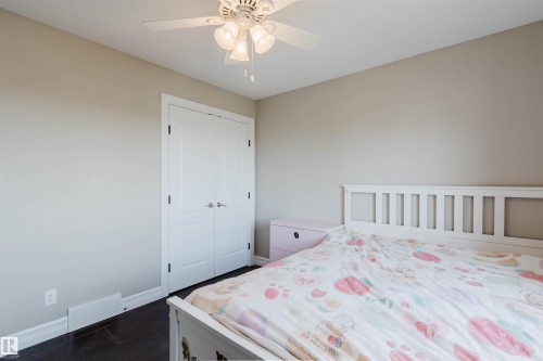 Bedroom featuring a ceiling fan with integrated lighting, a double-door closet with dark hardware, dark wood-finish flooring, and light-toned walls - 3412 Macneil Link, Edmonton, AB 