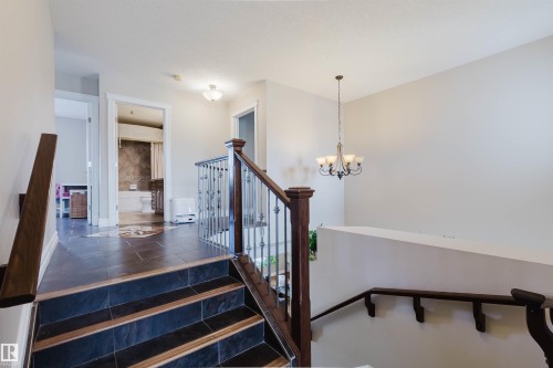 Split-level stairway featuring dark tile treads with wood-finish risers, a dark wood-finish handrail, and wrought-iron balusters - 3412 Macneil Link, Edmonton, AB 