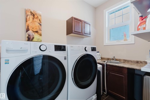 Dedicated laundry area featuring a utility sink, countertop space, dark wood-finish cabinetry, and a window - 3412 Macneil Link, Edmonton, AB 