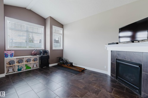 Living area featuring dark tile flooring, a fireplace with a dark tile surround and white mantel, and multiple windows with white blinds - 3412 Macneil Link, Edmonton, AB 