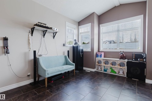 Spacious room featuring vaulted ceilings, multiple windows with white blinds, and dark rectangular floor tiles - 3412 Macneil Link, Edmonton, AB 
