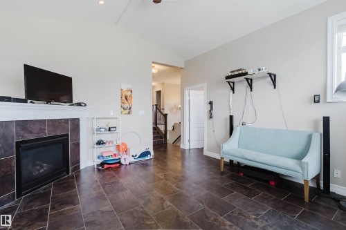 Spacious room featuring dark tile flooring, a fireplace with a tiled surround and white mantel, light-colored walls, and a high vaulted ceiling with recessed lighting - 3412 Macneil Link, Edmonton, AB 