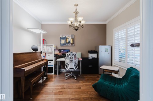 Interior space featuring wood-finish flooring, crown molding, a decorative chandelier, plantation shutters, and a two-tone wall treatment - 3412 Macneil Link, Edmonton, AB 