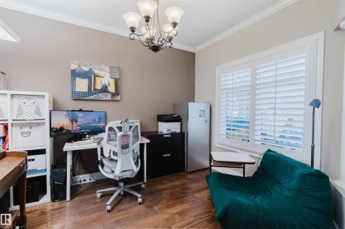 Bright room featuring wood-finish flooring, a white window with plantation shutters, crown molding, and a chandelier with glass shades - 3412 Macneil Link, Edmonton, AB 