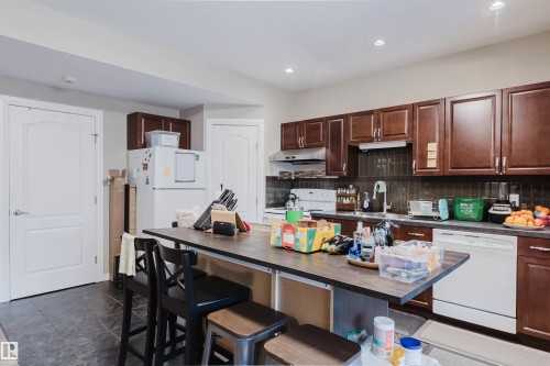 Kitchen featuring dark wood-finish cabinetry, dark tile backsplash, recessed lighting, and a kitchen island with seating - 3412 Macneil Link, Edmonton, AB 
