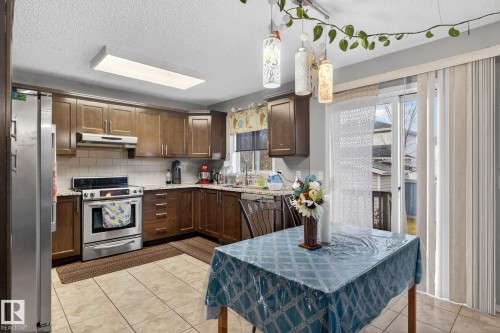 Kitchen and dining area featuring light-toned tile flooring, dark wood-finish cabinetry, stainless steel appliances, and a subway tile backsplash - 3912 31 Street, Edmonton, AB 