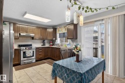 Kitchen and dining area featuring light-toned tile flooring, dark wood-finish cabinetry, stainless steel appliances, and a subway tile backsplash - 