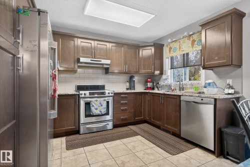 Kitchen featuring wood cabinetry, stainless steel appliances, granite-style countertops, subway tile backsplash, and tile flooring - 3912 31 Street, Edmonton, AB 