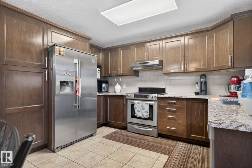 Kitchen featuring wood-finish cabinetry, stainless steel appliances, granite-style countertops, white subway tile backsplash, and ceramic tile flooring - 3912 31 Street, Edmonton, AB 
