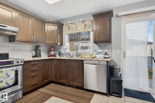 Kitchen featuring wood cabinetry, white subway tile backsplash, light-toned stone-finish countertops, stainless steel appliances, and a sliding glass door to the exterior - 3912 31 Street, Edmonton, AB 