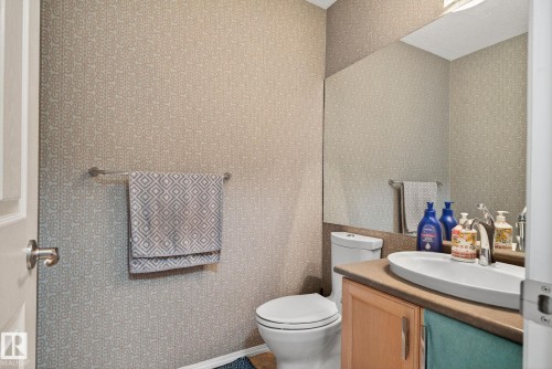 Powder room featuring patterned wallpaper, a wall-mounted mirror, and a vanity with an oval vessel sink and light wood cabinetry - 3912 31 Street, Edmonton, AB 