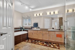 Bathroom featuring a built-in soaking tub with brown tile surround, an extended double vanity with light wood cabinetry, dual undermount sinks, and a large wall-mounted mirror - 