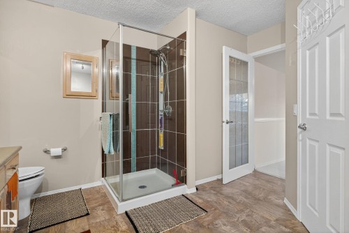 Glass-enclosed shower with brown and accent-tiled walls, wood-finish flooring, light tan walls, and a light wood vanity - 3912 31 Street, Edmonton, AB 