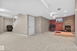 Spacious finished basement featuring light-toned carpeting and a corner fireplace with a stone surround - 