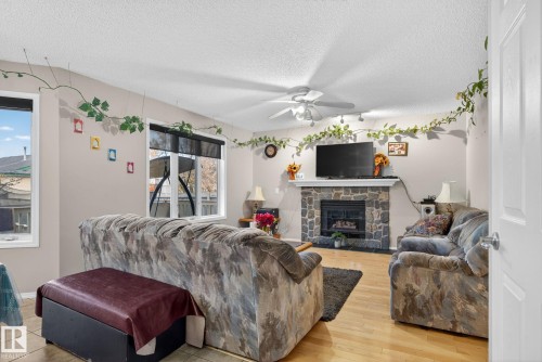 Living room featuring wood-finish flooring, a stone-faced fireplace with a white mantel, and multiple windows providing natural light - 3912 31 Street, Edmonton, AB 