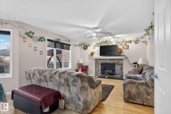 Living room featuring wood-finish flooring, a stone-faced fireplace with a white mantel, and multiple windows providing natural light - 