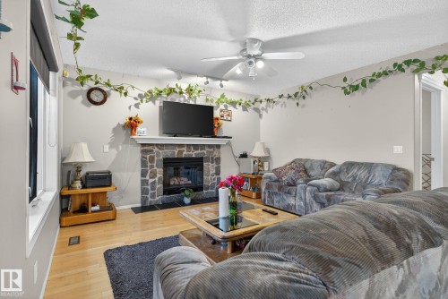 Living room featuring a stone-clad fireplace with a mantle, hardwood flooring, and a ceiling fan with integrated lighting - 3912 31 Street, Edmonton, AB 