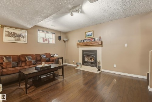 Inviting living area featuring rich wood-finish flooring, a contemporary fireplace with a stone surround, and a substantial wood mantel - 18648 57 Avenue, Edmonton, AB - Indoor Photo Showing Living Room With Fireplace
