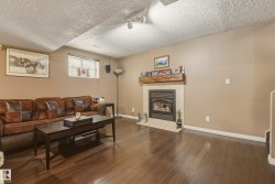 Inviting living area featuring rich wood-finish flooring, a contemporary fireplace with a stone surround, and a substantial wood mantel - 