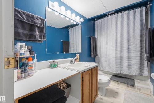 Bathroom featuring a single vanity with wood-finish cabinetry, a mirror with vanity lighting, and a bathtub with a shower curtain - 18648 57 Avenue, Edmonton, AB - Indoor Photo Showing Bathroom