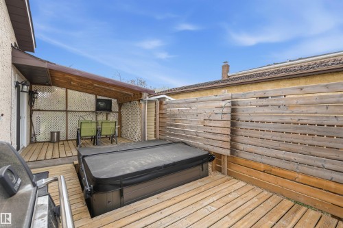 Outdoor wooden deck featuring an integrated hot tub with a protective cover, a covered patio area with lattice screens, and a privacy fence - 18648 57 Avenue, Edmonton, AB - Outdoor With Deck Patio Veranda With Exterior