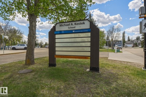 Brown and white school signage with multiple blank information panels, set on a grassy area with a mature tree - 18648 57 Avenue, Edmonton, AB - Outdoor