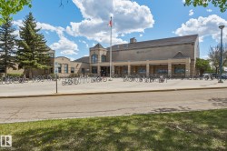 Brick building exterior with a flag pole, multiple bicycle racks, and mature evergreen trees - 