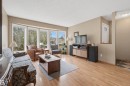 Spacious living area featuring large bay windows, wood-finish flooring, neutral wall tones, and a built-in media console - 18648 57 Avenue, Edmonton, AB  - Indoor Photo Showing Living Room 