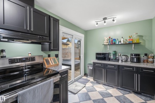 Kitchen featuring dark cabinetry, speckled countertops, stainless steel range, track lighting, and checkerboard flooring - 18648 57 Avenue, Edmonton, AB - Indoor Photo Showing Kitchen