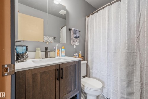 Bathroom vanity featuring a white rectangular undermount sink, dark wood-finish cabinetry with black hardware, and a white countertop - 18648 57 Avenue, Edmonton, AB - Indoor Photo Showing Bathroom