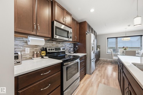 Contemporary kitchen featuring dark wood cabinetry, stainless steel appliances, light-toned countertops, and a mosaic tile backsplash - 3457 Cutler Crescent, Edmonton, AB - Indoor Photo Showing Kitchen With Double Sink With Upgraded Kitchen