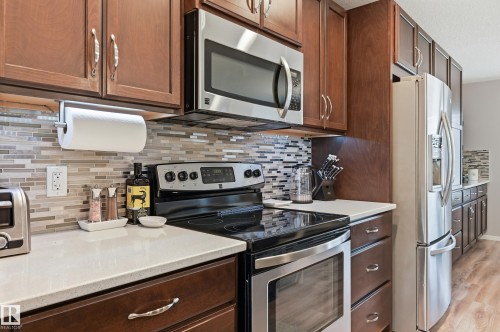 Kitchen featuring dark wood-finish cabinetry, stainless steel appliances, a multi-tone mosaic tile backsplash, and light-colored countertops - 3457 Cutler Crescent, Edmonton, AB - Indoor Photo Showing Kitchen