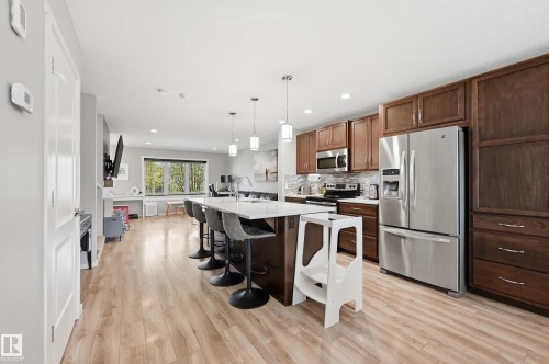 Spacious kitchen featuring an expansive center island with seating, stainless steel appliances, dark wood cabinetry, and wood-finish flooring throughout - 3457 Cutler Crescent, Edmonton, AB - Indoor Photo Showing Kitchen With Upgraded Kitchen