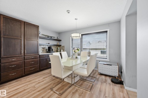Dining area featuring wood-finish flooring, a built-in dark wood cabinetry wall, white countertops, and a mosaic tile backsplash - 3457 Cutler Crescent, Edmonton, AB - Indoor Photo Showing Dining Room